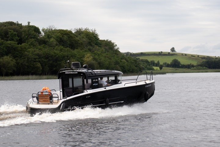Black boat speeding on a lake with green hills in the background.