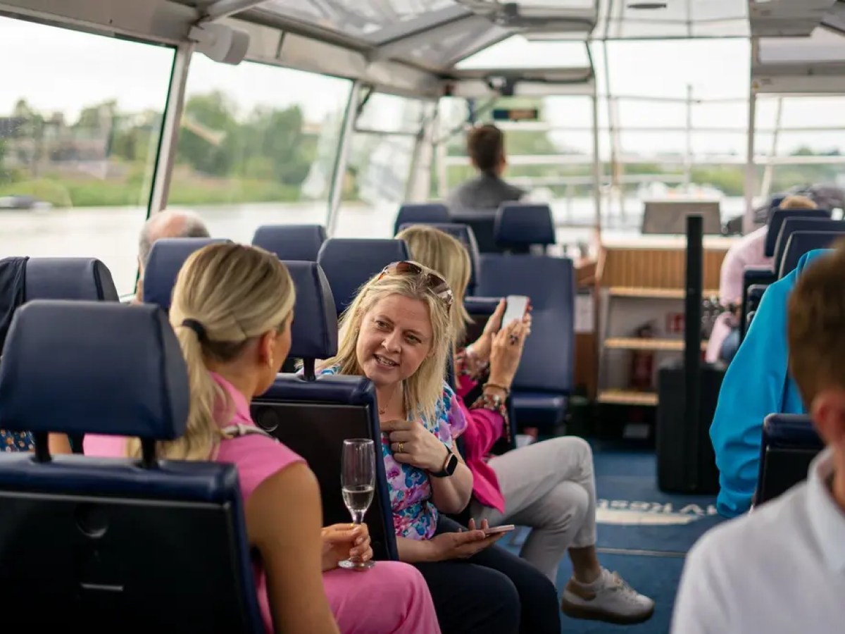 People seated on a boat, talking and enjoying the view outside large windows.