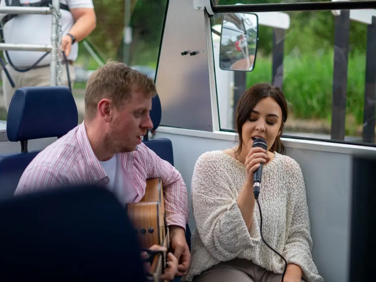 Man playing guitar and woman singing with a microphone on a boat.