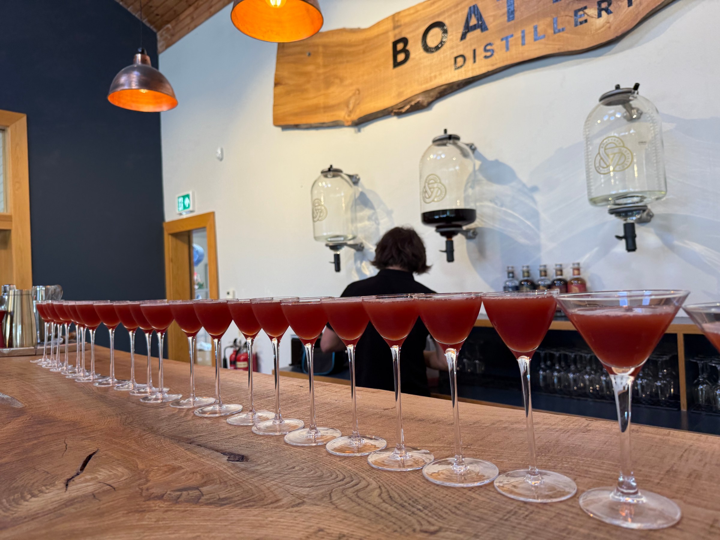 Row of cocktail glasses with red drinks on a wooden bar counter in a distillery.